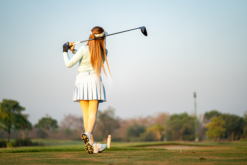 Asian woman swings golf club on golf course