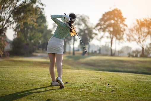 Asian woman swings golf club on golf course