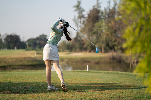 Asian woman swings golf club on golf course