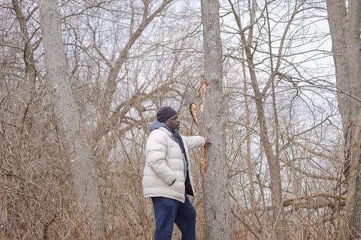 A black man standing among the trees and looking.