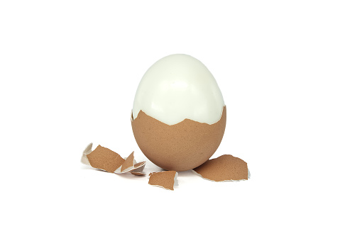 Egg in the process of being peeled, around it lay scattered pieces of eggshell, isolated on white background