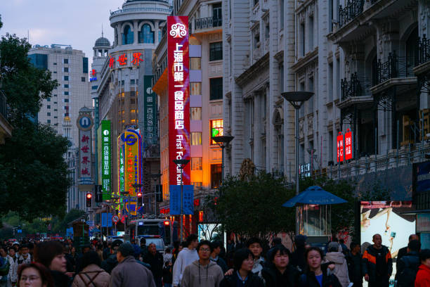 Shanghai, China - March 15th 2024: Crowds walk below neon signs on Nanjing Road. The street is the main shopping district of the city and one of the world's busiest shopping districts.