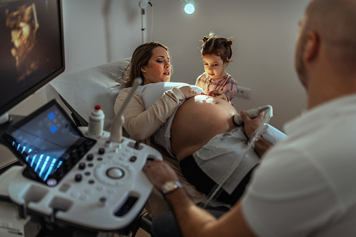 a pregnant woman visiting a gynecologist while her daughter is holding her for support