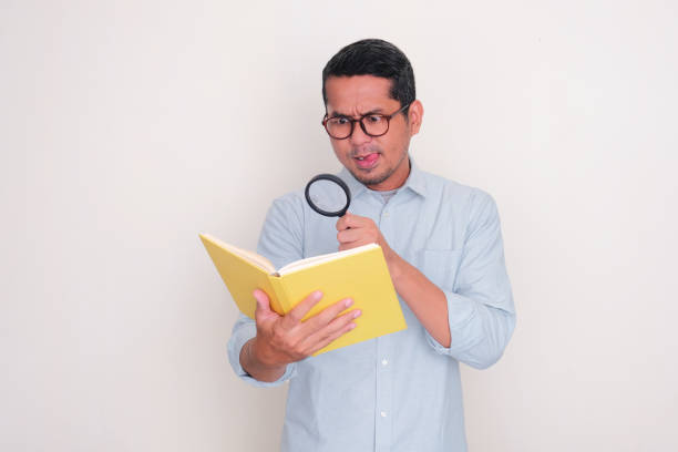 istock Adult Asian man searching something inside a book using magnifying glass 2095627064