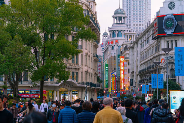 Shanghai, China - March 15th 2024: Crowds walk below neon signs on Nanjing Road. The street is the main shopping district of the city and one of the world's busiest shopping districts.