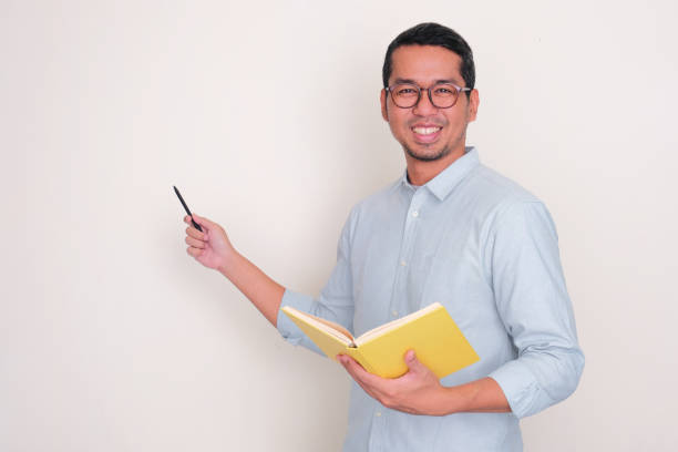 istock A lecturer smiling at the camera while holding a book and pointing beside 2095647728
