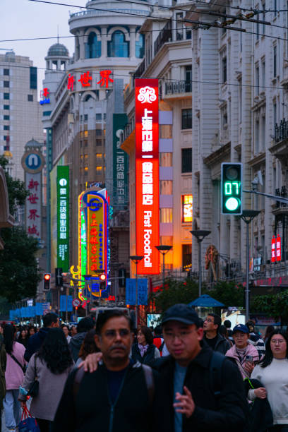 Shanghai, China - March 15th 2024: Crowds walk below neon signs on Nanjing Road. The street is the main shopping district of the city and one of the world's busiest shopping districts.