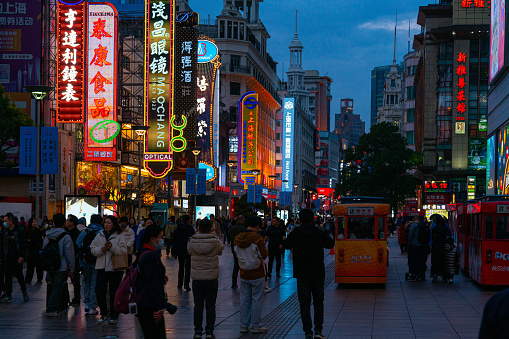 Shanghai, China - March 15th 2024: Crowds walk below neon signs on Nanjing Road. The street is the main shopping district of the city and one of the world's busiest shopping districts.