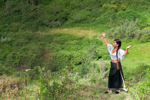 Cheerful indigenous woman from Ecuador celebrating the beauty of nature in a thanksgiving ritual in a lush green field during the day