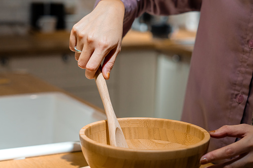 a woman's hand holding a wooden spatula making dough with a wooden bowl, close-up shot in the kitchen