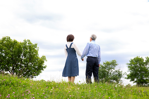 Back view of a middle-aged Japanese couple, holding hands in the park, full body,