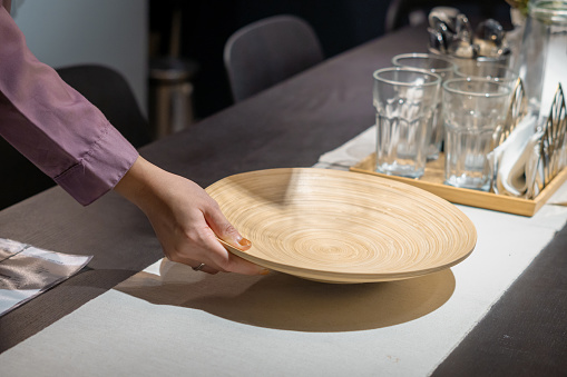 Illustration of woman's hand placing brown wooden plate on dining table