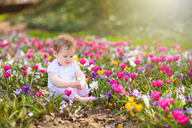 Cute little girl in pink dress playing in blooming spring park with first white wild anemone flowers. Child on Easter egg hunt in blooming garden. Kids play outdoor picking flower bouquet.