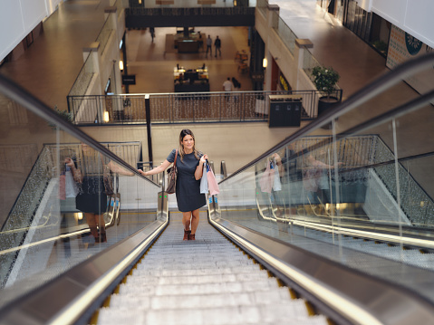 Above view of happy businesswoman moving up with escalator in a shopping mall. Photographed in medium format.