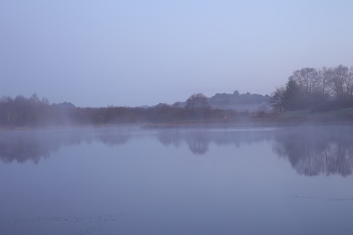 A tranquil lake with mist over water and distant trees