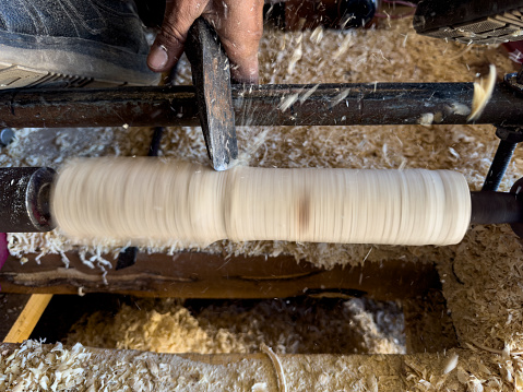 Carpenter shaping a piece of wood with wood turning and lathe flying away chips at high speed