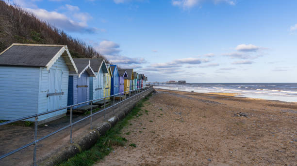 beach huts on the beach with the pier in the background in cromer, norfolk, england, uk - beach hut beach cromer hut 뉴스 사진 이미지