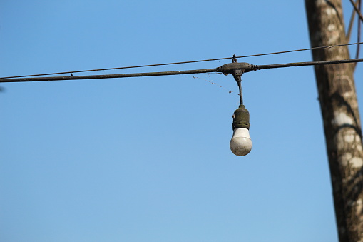 Old-school light bulb with stretched wires against the background of a bright blue sky in the morning