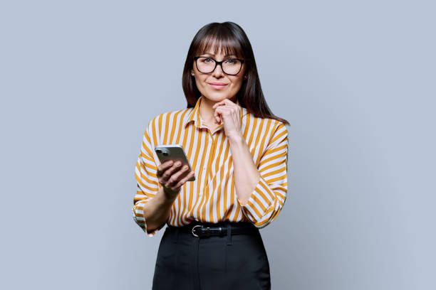 istock Middle aged smiling woman with smartphone on grey studio background 2095906628