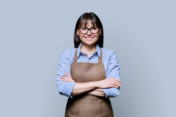 istock Confident smiling middle-aged woman in apron on gray background 2095907194
