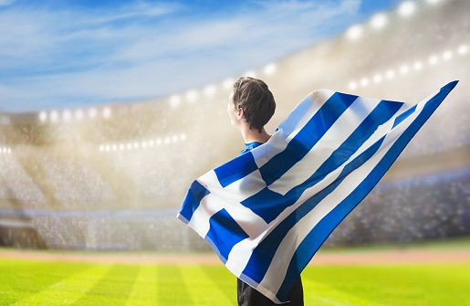 Greece football supporter on stadium. Greek fans on soccer pitch watching team play. Group of supporters with flag and national jersey cheering for Greece. Championship game.