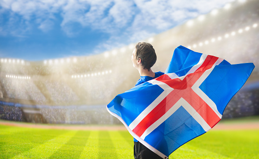 Iceland football supporter on stadium. Icelandic fans on soccer pitch watching team play. Group of supporters with flag and national jersey cheering for Iceland. Championship game.