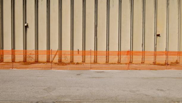 Safety temporary orange plastic netting fence for construction industry in front of a large concrete block wall. Background and texture. Copy space.