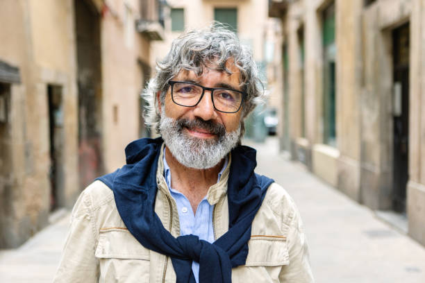 Smiling portrait of senior 60s middle aged man looking at camera. Happy mature male standing outdoors. Outside head shot at city street.