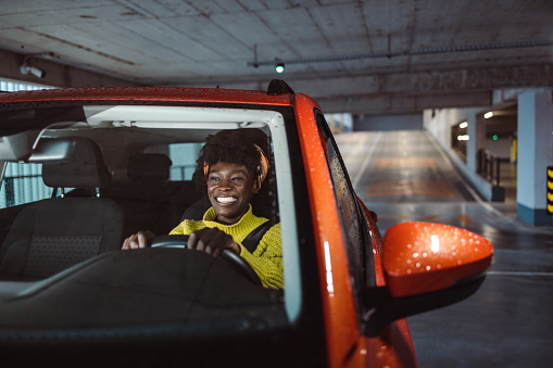 Front view of smiling young African American woman driving orange car and smiling