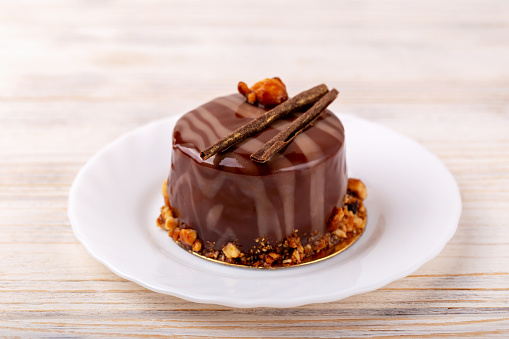Fresh delicious chocolate cake on plate on white wooden background. Caramel glaze and decoration add appeal and desire