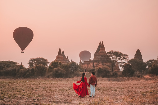 Couple stands watching balloons float at Bagan temple in Myanmar archaeological zone in the morning.