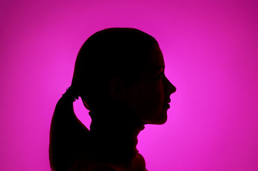 Profile of a dark female silhouette on a purple background close up.