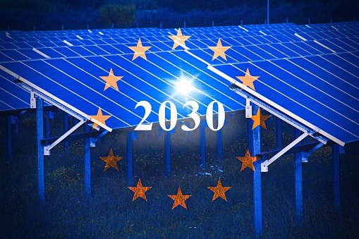 Official flag of the European Union in front of a large array of solar panels, with text 2030 .