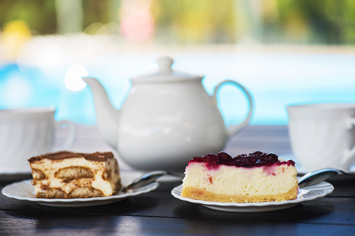 Afternoon tea set with hot tea and tasty cakes on the table and the swimming pool. Hotel resort or resting concept