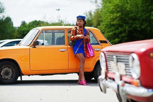 Beautiful african american lady with shopping bags standing near orange classic retro car.