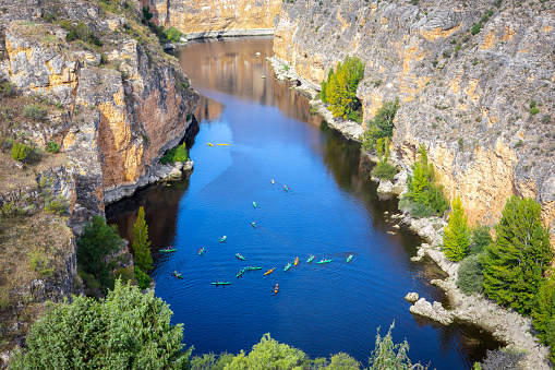 Hoces del Rio Duraton Nature Reserve (Parque Natural de las Hoces del Río Duratón) with limestone vertical cliffs, blue water and colorful kayaks floating.