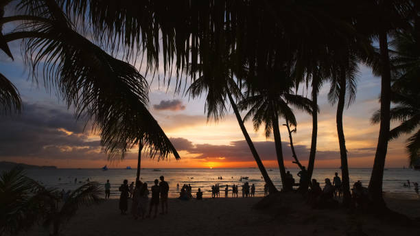 istock Sunset on beach with people and palms 2096027801