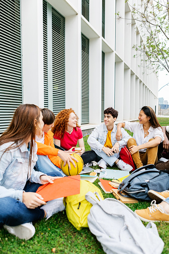 Students of ethnic diversity sitting on the campus lawn with educational and recreational materials, such as a basketball. Campus life and youth