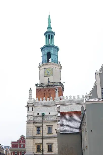 A photo of the old market square in Pozna, Poland, taken in January during winter. Snow-covered rooftops with the historic town hall against a white sky backdrop.