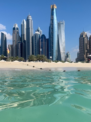 Beautiful day view on Dubai Marina Promenade, palms, modern Towers with floating yachts and boats from bridge timelapse, United Arab Emirates. Dubai Marina is a district in Dubai and an artificial canal city. Blue cloudy sky