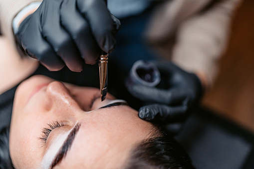 Female beautician microblading her female client's eyebrows at the beauty salon.