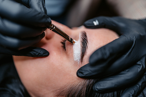 Female beautician microblading her female client's eyebrows at the beauty salon.