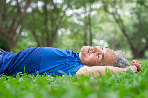 sporty senior man lying down on grassess and taking a nap while resting in park,adequate sleep during the day help elderly body to rest and restore strength to help carry out daily activities normally