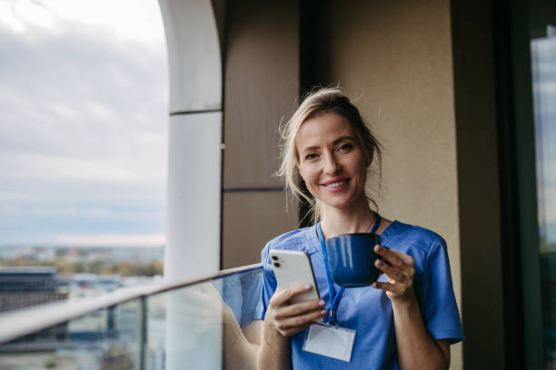 istock Nurse, doctor in uniform taking break, standing on hospital balcony, drinking coffee, scrolling on smartphone. Work-life balance of healthcare worker. 2096115870