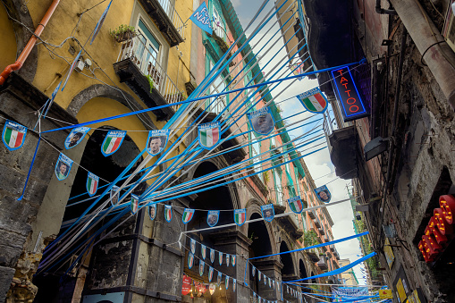 Narrow downtown Naples street decorated with local soccer team colors, recent Italian league champions; low angle view.