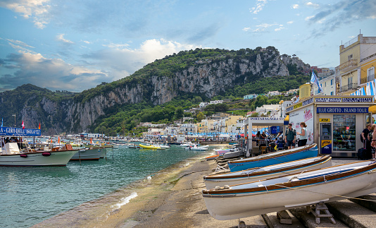 Coastal view of the island of Capri, Italy, a popular tourist destination year round, with boats and bars on the beach.