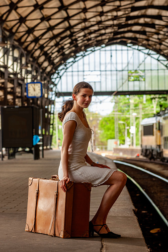 Woman Waiting in Railway Station platform sitting on a suitcase. A retro style shot.