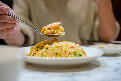 In the cropped image, a woman is seen enjoying shrimp and egg fried rice at a Chinese restaurant