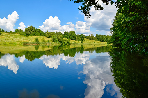 Lake in a green summer forest. Clouds are reflected in the water. Beautiful natural landscape. Weather.