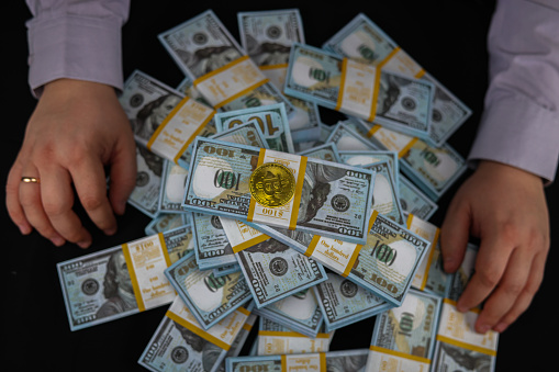 A trader holds his hands on either side of a stack of dollar bills with a bitcoin coin on top. The trader earned a large amount of money on the cryptocurrency exchange by selling and buying Bitcoin..